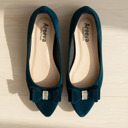 Pair of blue pointed-toe shoes with bow and gemstone detail on a light wooden surface, branded 'Areeya Collection'.