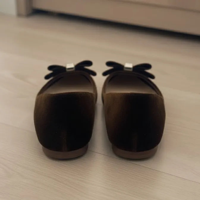 Pair of brown loafers with decorative bows on a light wooden floor.