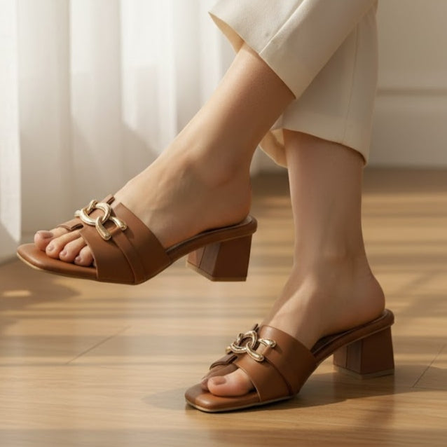 Brown sandals with gold buckles worn by a person on a wooden floor.