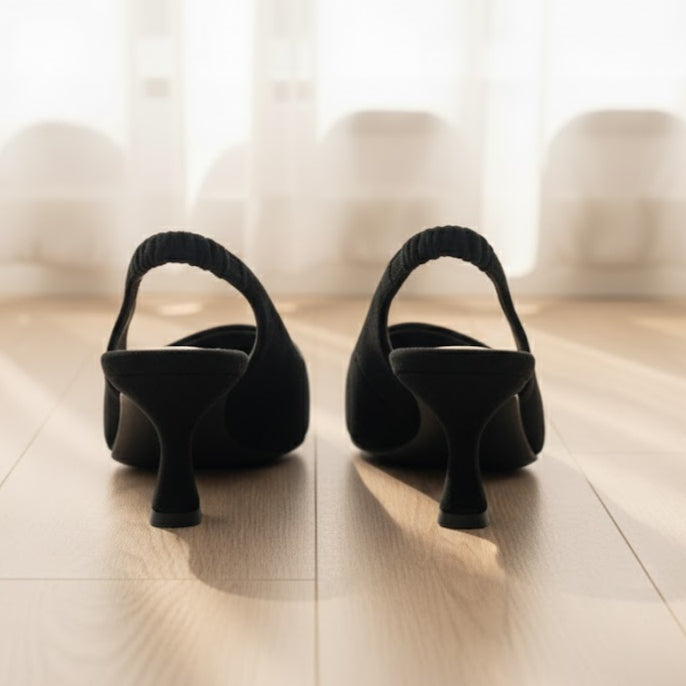 Pair of black high-heeled shoes on a wooden floor with a blurred curtain background