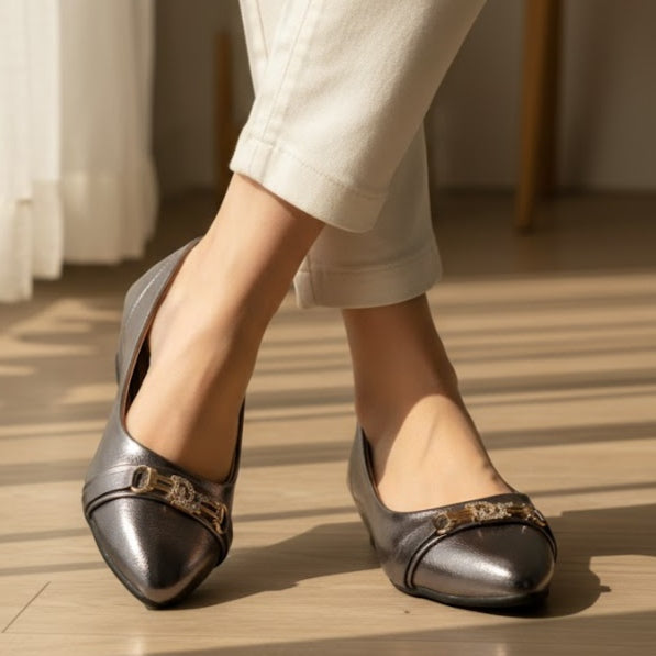gray flat shoes with decorative elements worn by a person on a wooden floor.