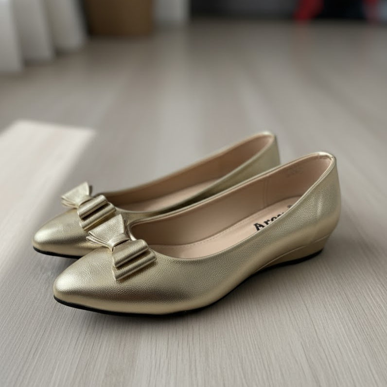 Pair of gold shoes with bow details on a light wooden floor.