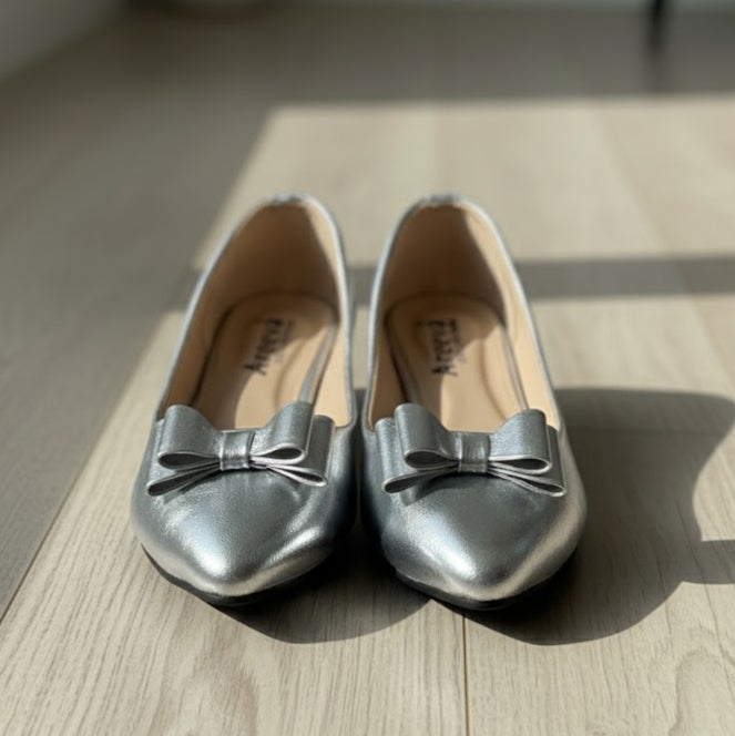 Pair of silver shoes with bow details on a wooden surface