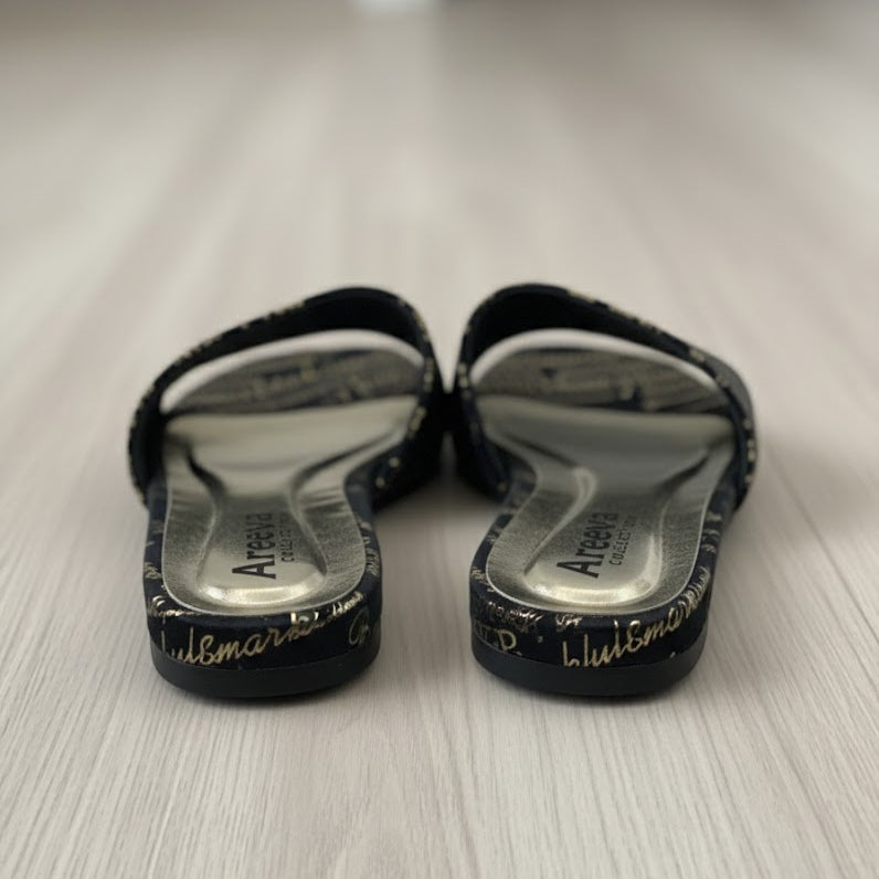 Pair of black sandals with white soles on a light wooden floor.