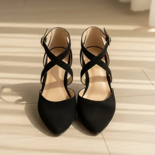 Pair of black shoes with criss-cross straps on a light wooden floor.
