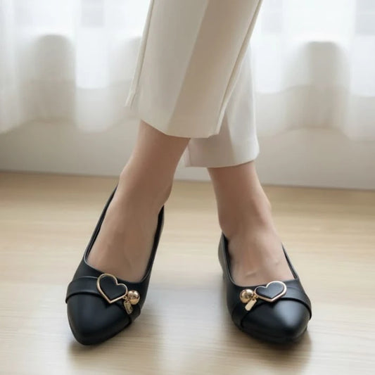 Black shoes with heart-shaped embellishments worn by a person on a light wooden floor.