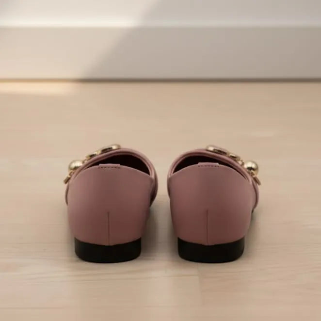 Pair of pink loafers with gold accents on a light wooden floor.