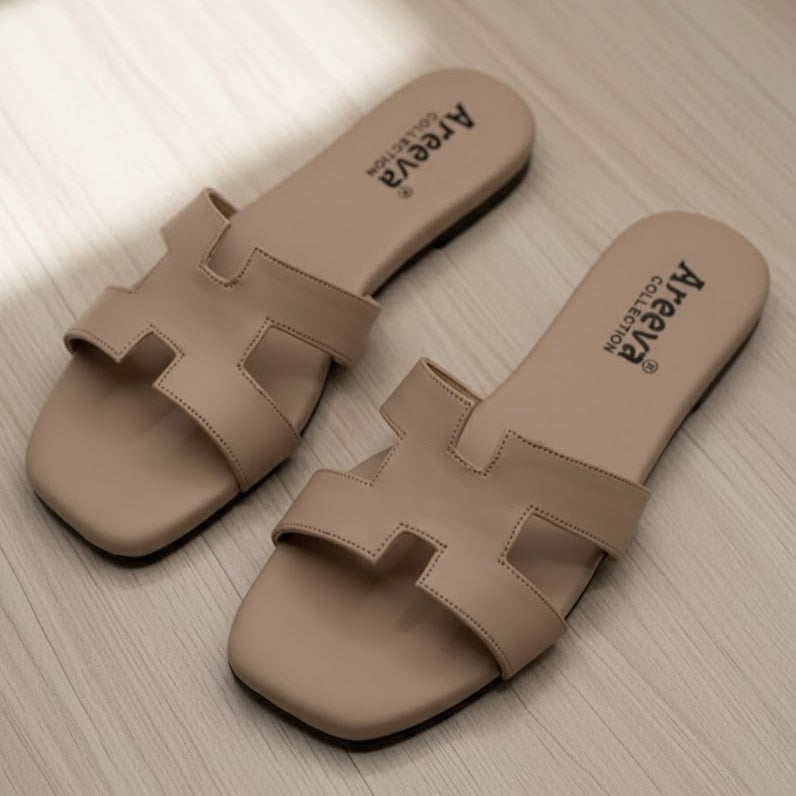 Pair of beige slides with 'Apevva' branding on a light wooden floor.