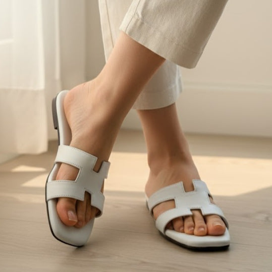 White sandals worn indoors on a light wooden floor.