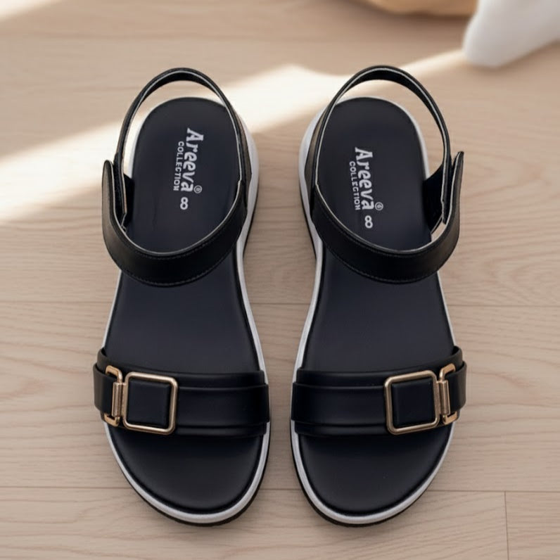 Black sandals with gold buckles on a wooden surface, featuring the Areena Collection logo.