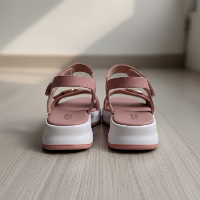 Pair of pink sandals with white soles on a wooden floor.