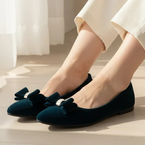 Navy blue flats with bow details worn by a person on a light wooden floor.