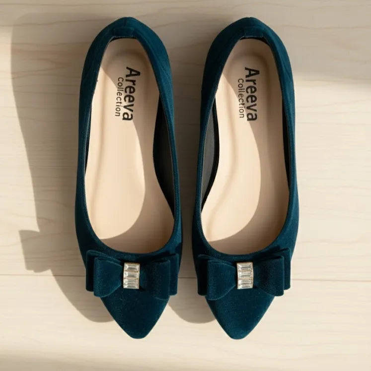 Pair of blue pointed-toe shoes with bow and gemstone detail on a light wooden surface, branded 'Areeya Collection'.