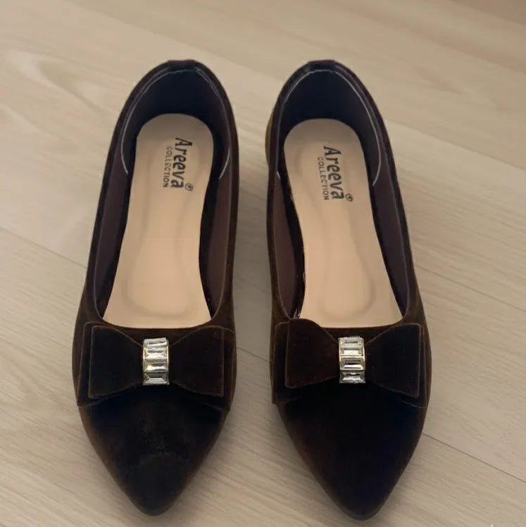 Pair of brown shoes with a bow and silver accents on a light wooden surface.