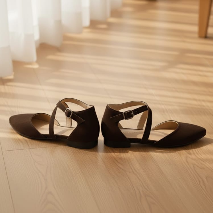 Pair of brown sandals on a wooden floor with white curtains in the background