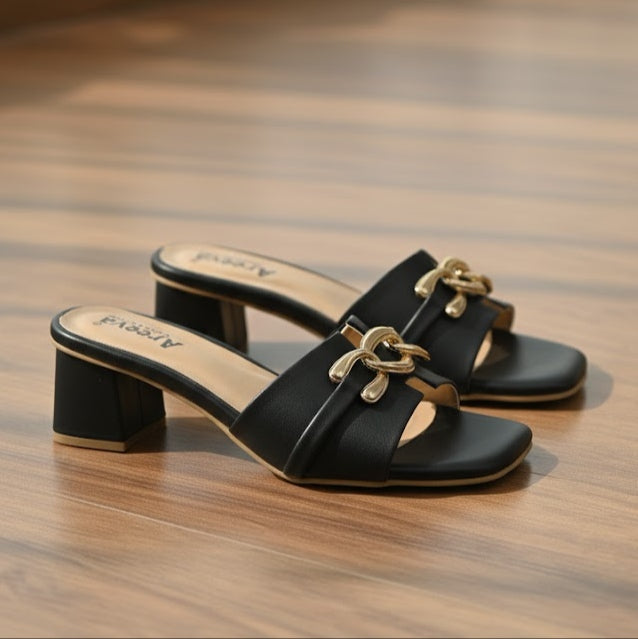Black sandals with gold accents on a wooden floor