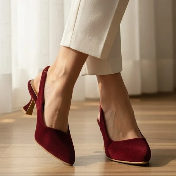 Red high-heeled shoes worn with white pants on a wooden floor.