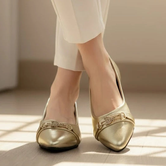 Gold shoes with embellishments worn by a person in a neutral setting