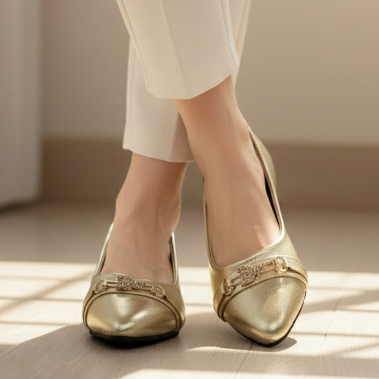 Gold shoes with embellishments worn by a person on a neutral background