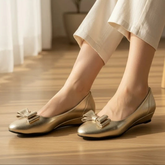 Gold shoes with bows worn by a person on a wooden floor.