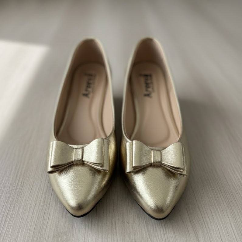 Pair of gold shoes with bow details on a neutral background