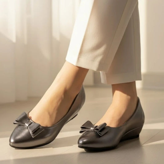 Gray shoes with bow details worn by a person in light-colored pants on a neutral background