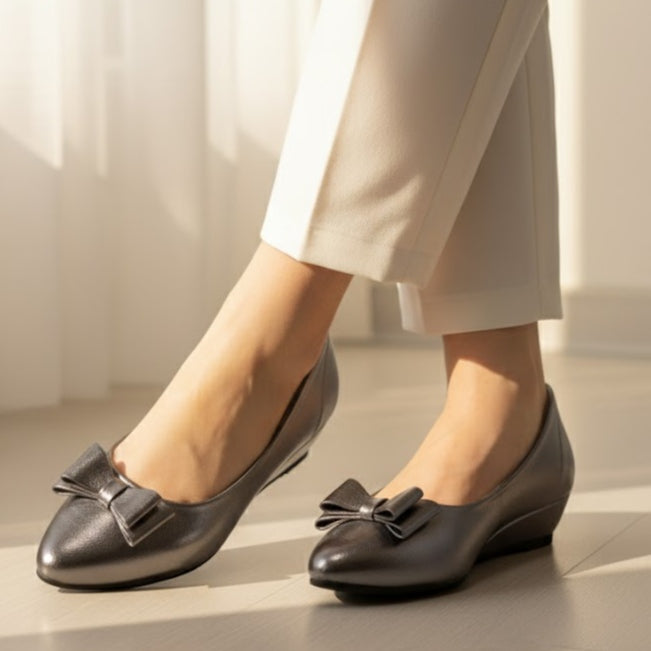 Gray shoes with bow details worn by a person on a light wooden floor.