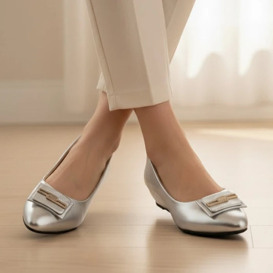 Silver shoes with a bow detail worn by a person on a light wooden floor.