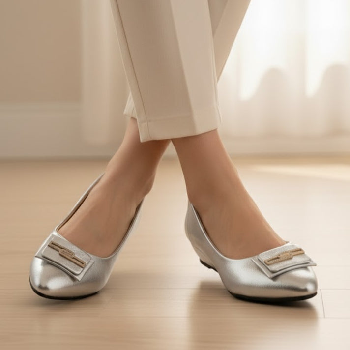 Silver shoes with bow details worn by a person on a light wooden floor.