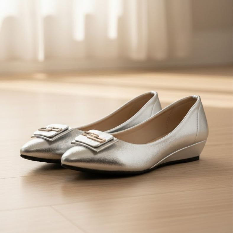 Pair of silver shoes with decorative buckles on a wooden floor.