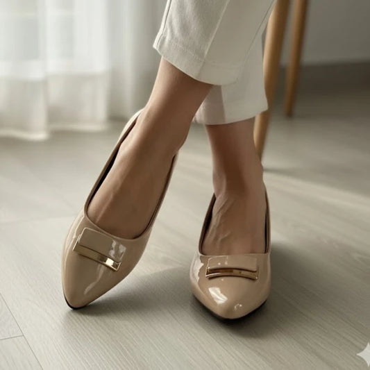 Beige shoes with gold accents worn by a person on a light wooden floor.