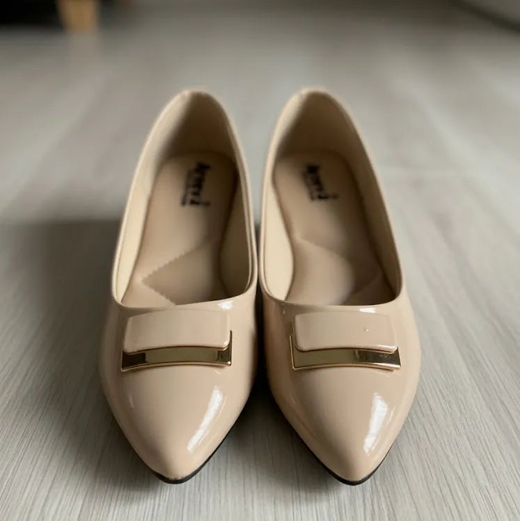 Pair of beige shoes with gold accents on a light wooden floor.