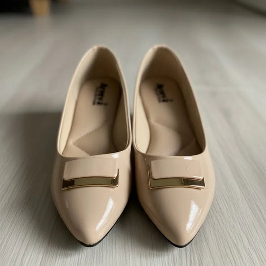 Pair of beige shoes with gold accents on a light wooden floor.