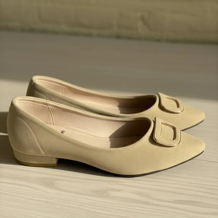 Pair of beige shoes with a decorative buckle on a wooden surface