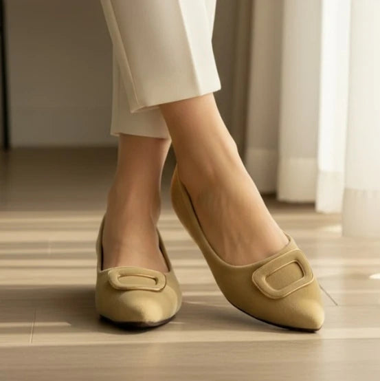 Beige shoes worn with white pants on a wooden floor.