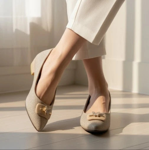 Beige flat shoes with decorative bows worn by a person in a light setting.