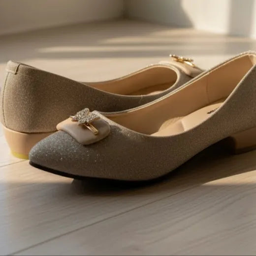 Pair of beige high-heeled shoes with decorative buckles on a light wooden floor.