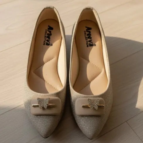 Pair of glittery shoes with decorative bows on a wooden floor.