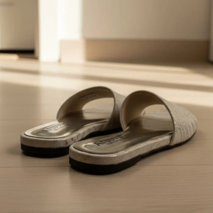 Pair of beige slides with black soles on a wooden floor.