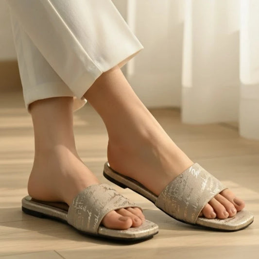 Person wearing light gray slippers on a wooden floor with white pants.