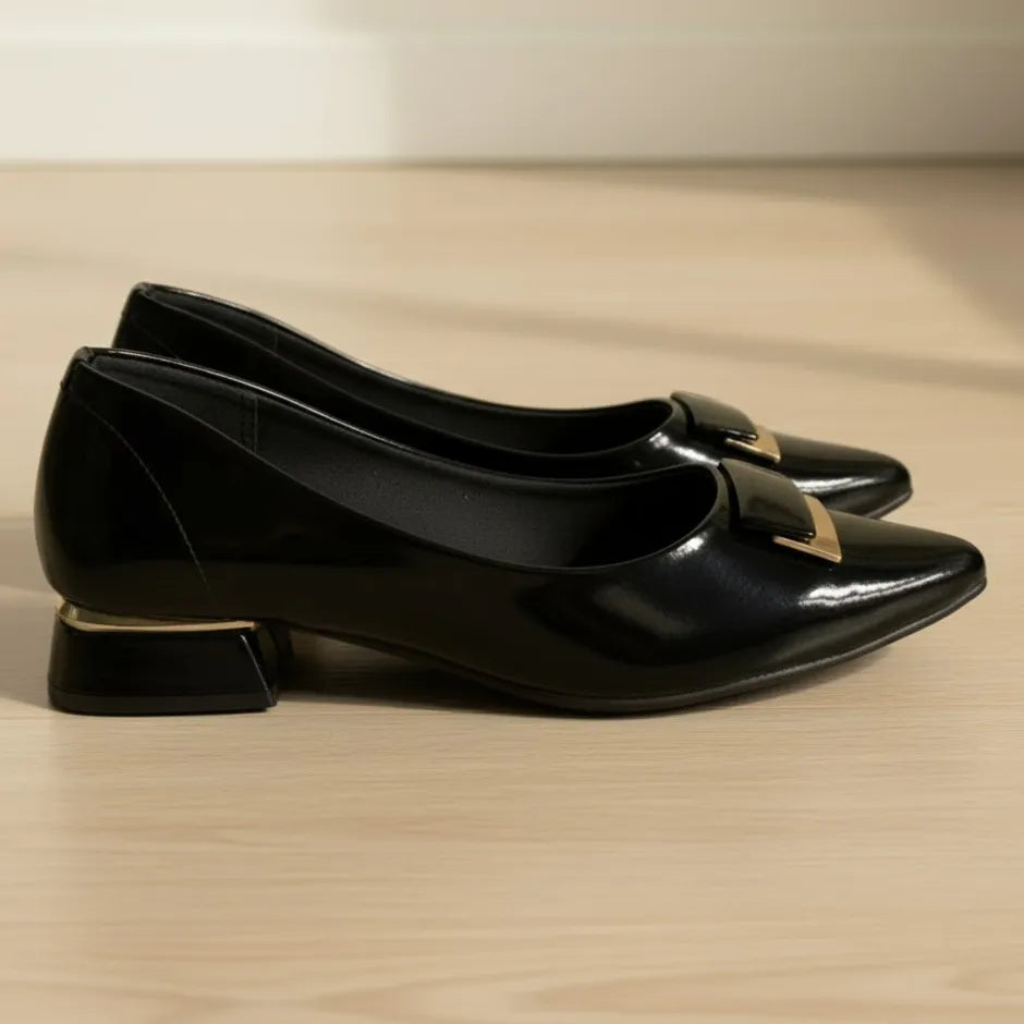 Black patent leather shoes with gold accents on a wooden surface