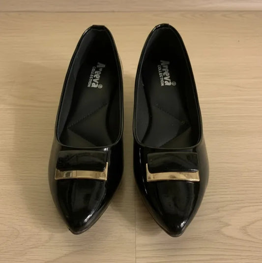 Pair of black shoes with gold buckles on a wooden surface