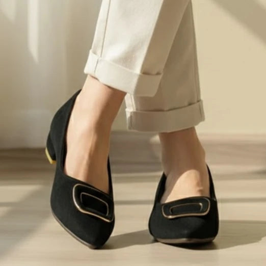 Black flats worn with light-colored pants on a neutral background