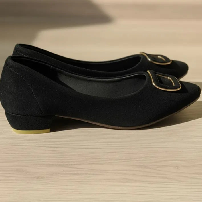 Pair of black shoes with gold buckles on a beige surface