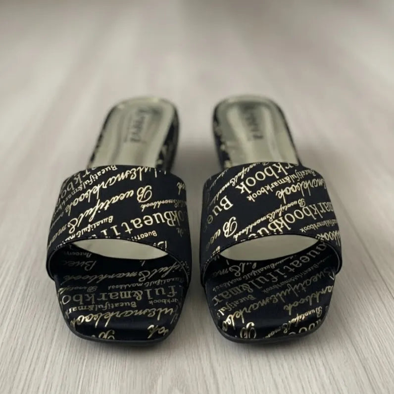 Pair of black slides with white text on a light wooden floor.