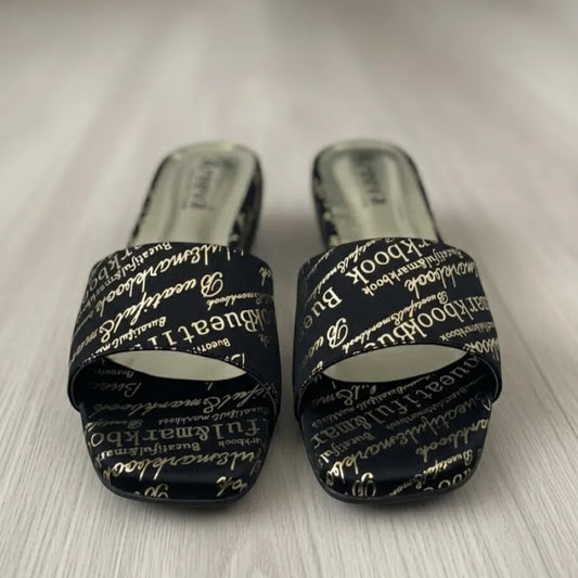 Pair of black slides with white text on a light wooden floor.