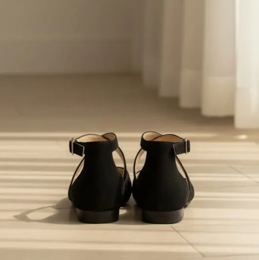 Pair of black sandals on a light wooden floor with a neutral wall background
