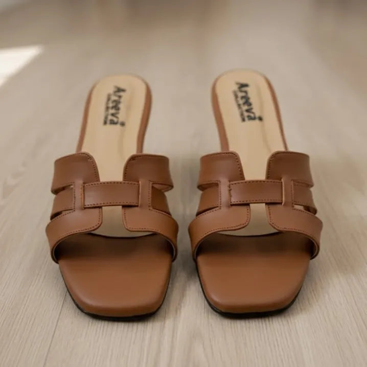 Pair of brown slipper with branding of Areeva  on a light wooden floor.