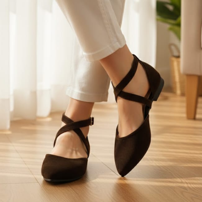 Brown dance shoes worn with white pants on a wooden floor.