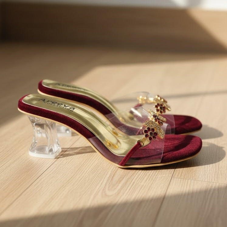 Red high-heeled shoes with clear heel and gold embellishments on a wooden surface
